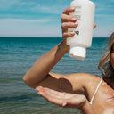 Ocean view woman applying Sea Salt Body Sculpt Kit's Multi-Mineral Cleanser with honey-like pour in hand.