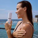 Woman holding a bottle of Bronte skincare by the beach