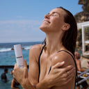 Woman at the beach holding a bottle of Bronte 3-in-1 Hydrating Milk